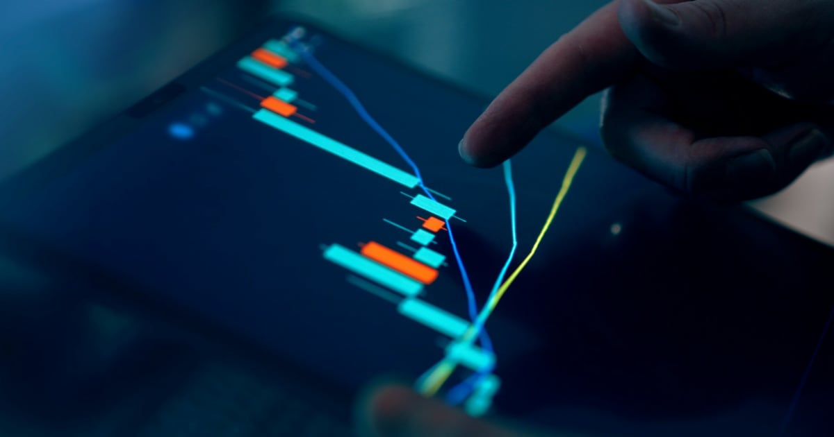 A finger tracing a candlestick price chart with trend lines on a dark tablet screen