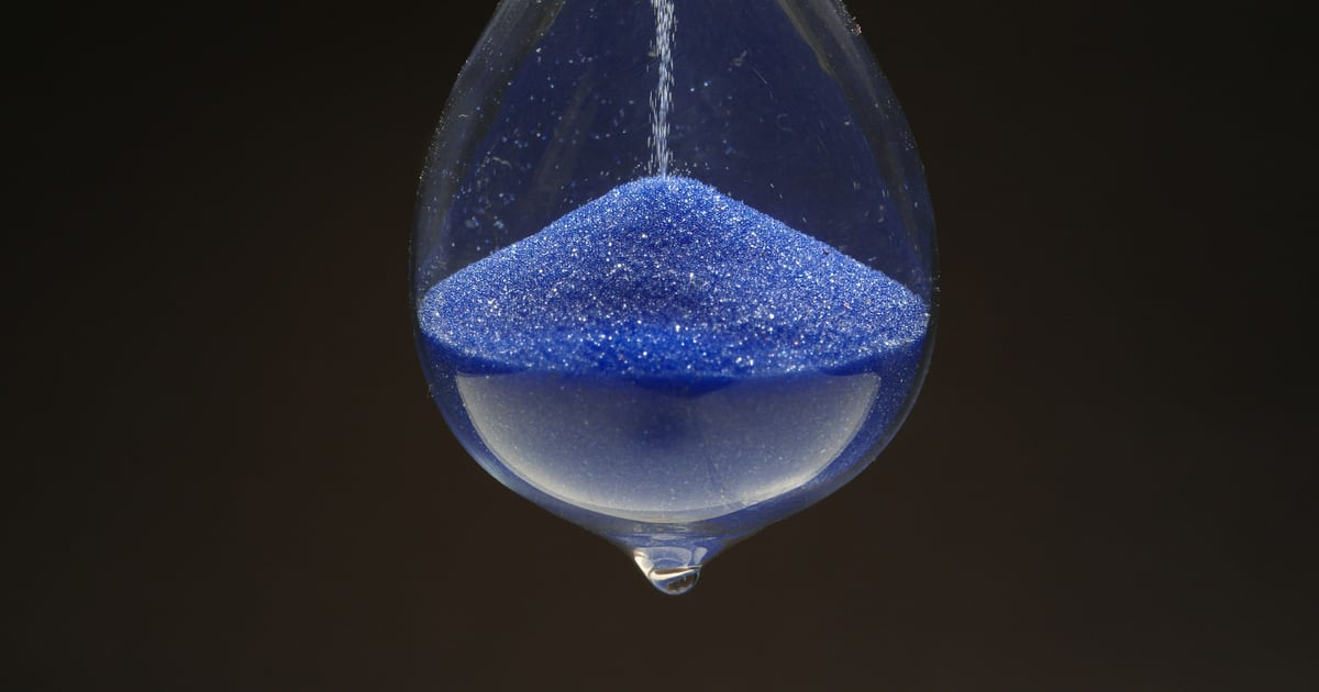 Blue sand running through an hourglass against a dark background