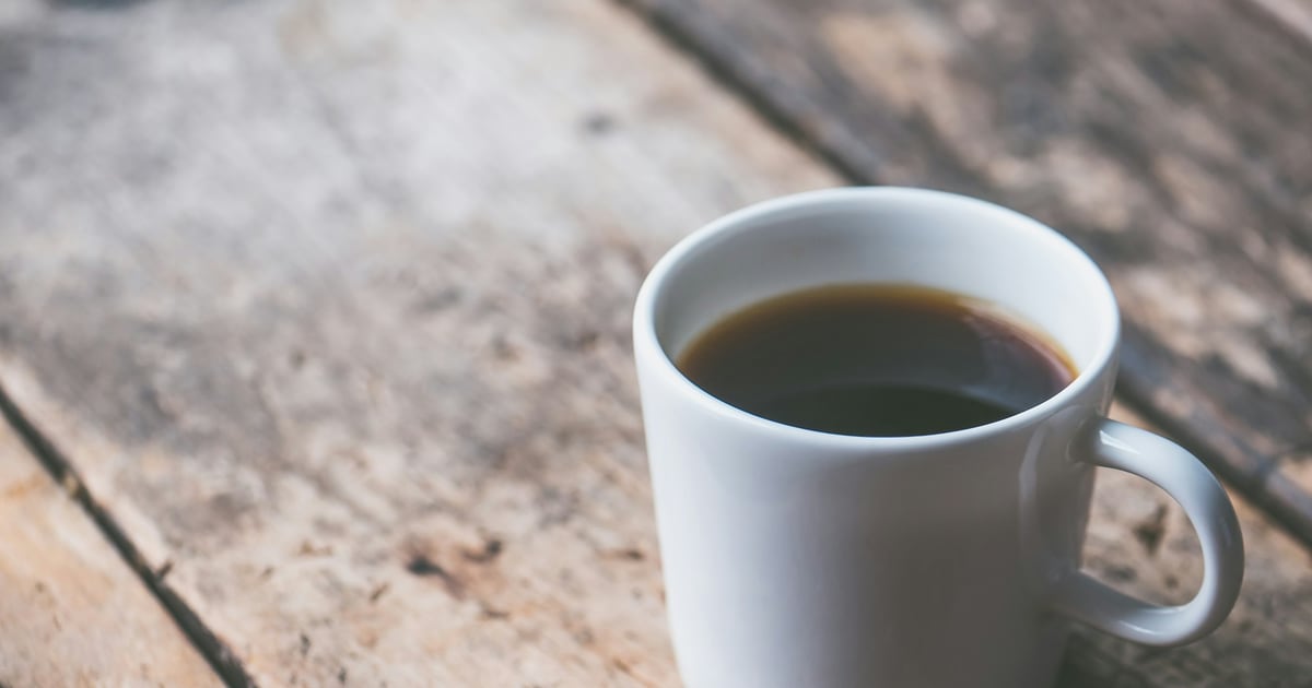 A white mug of black coffee with its handle turned toward the camera on a weathered wooden table
