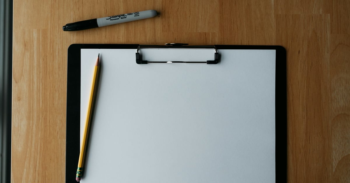 A blank sheet on a clipboard with a pencil, on a wooden desk