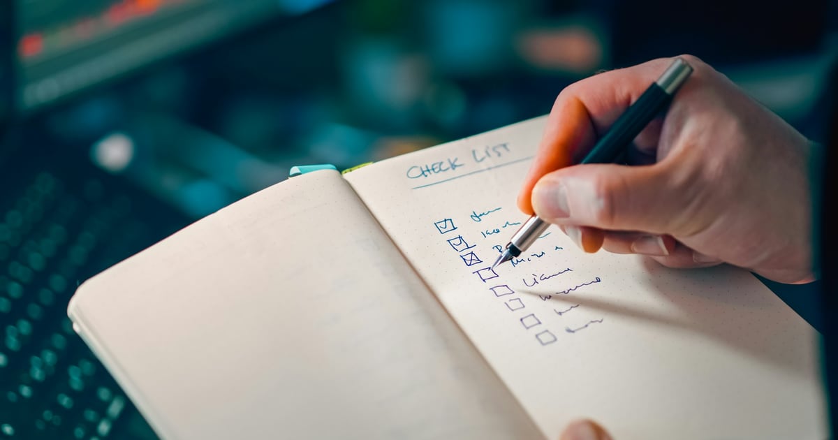 A hand ticking boxes on a handwritten checklist in a notebook