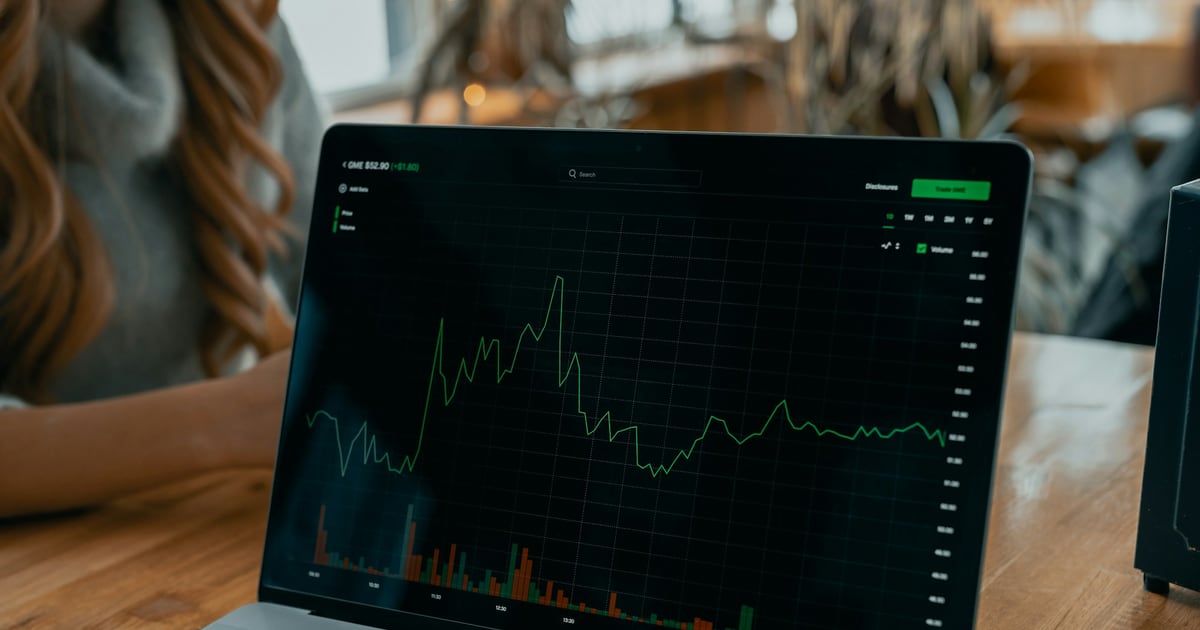 A laptop on a café table showing a green intraday price chart