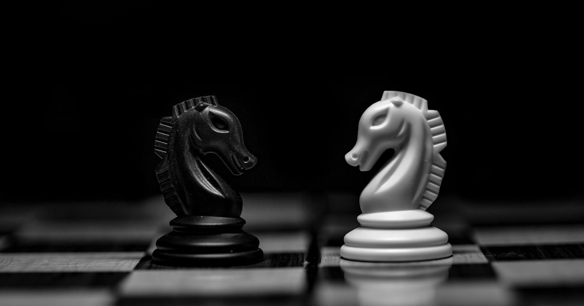 A black knight and a white knight facing each other on a dark chessboard