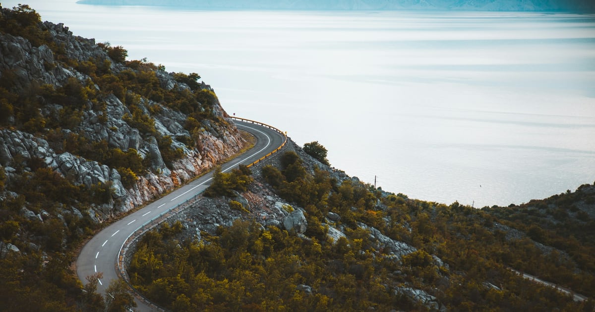 A narrow road winding down a rocky hillside toward the sea