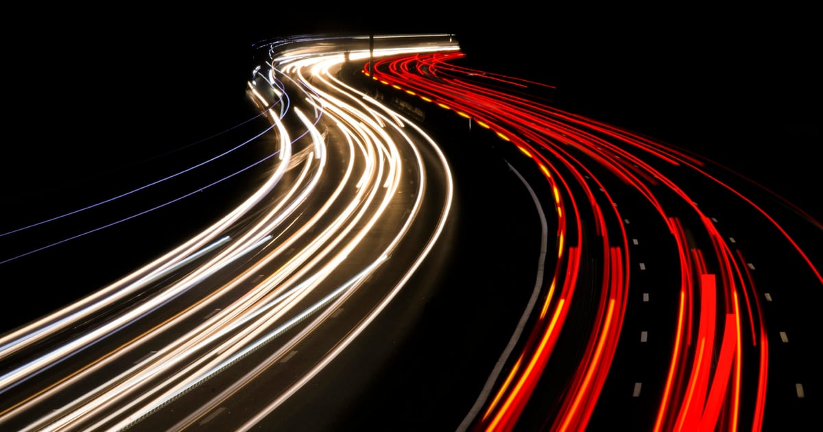 Long-exposure light trails from traffic sweeping around a curve at night